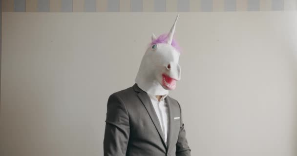 オフィスの職場で彼の財政的な成功を楽しんでいるスーツでユニコーンマスクを持つおかしい男 ユニコーンマスクを持った男 ビジネスススーツの満足した上司 給与や利益の概念について — ストック動画