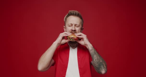 Omul Caucazian Netăiat Mănâncă Burger Carne Plăcere Fundal Roșu Izolat — Videoclip de stoc