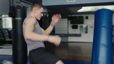 Sporcu adam spor salonunda spor yapar ve boks torbasını yumruklar. Spor kulübünde spor yapan genç erkek boksör. Kickboks eğitim konsepti.