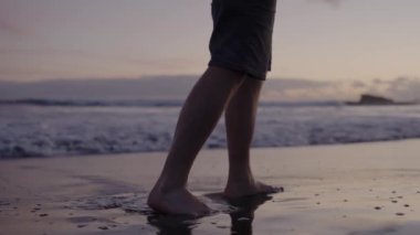 Gün batımında deniz kıyısında yürüyen adamı gördüm. Yaz günü okyanus kıyısında çıplak ayaklı erkek bacaklarına yakın çekim. Tatil kavramı