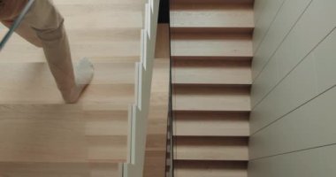 Manzaralı adam modern evdeki ahşap merdivenlere iniyor. Erkek bacakları apartmanda merdivenlere basıyor.