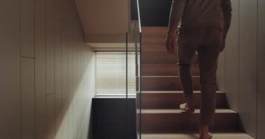 Çıplak ayaklı bir adamın manzarası modern evin ikinci katına çıkıyor. Erkek, çağdaş apartmandaki merdivenlere çıkıyor.
