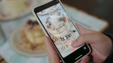 Erkek ellerindeki kırpılmış görüntü, kafedeki akıllı telefonu kullanarak Japon gözlemesinin fotoğrafını çekiyor. Adam cep telefonu kamerasıyla pofuduk krep fotoğrafı çekiyor. Sosyal medya içeriği için tatlı fotoğrafı