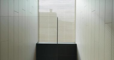İçerideki detaylar, güneş panjurlu pencere, cam bariyer ve modern evdeki beyaz ahşap panellerle süslenmiş duvar. Dairedeki pencereden güneş ışığı