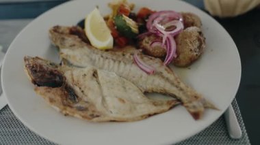 Tabakta kızarmış balık, sebze, soğan ve kafeterya masasında taze limon olsun. Lokantada deniz ürünleriyle lezzetli ve sağlıklı bir öğle yemeği. Akdeniz mutfağı