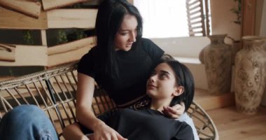 Arkadaşlık kavramı. LGBT hakları, lezbiyen ailesi. Düşük açılı bir el kamerası ile çekilen genç lezbiyen çift, evdeki ışıklı oturma odasının penceresinde kanepede otururken gülümsüyor ve nazikçe el ele tutuşuyor..