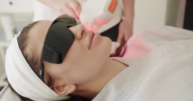 Koruyucu gözlüklü güzel kadın güzellik kliniğinde LPG donanım masajı yaptıran kadın. Bir tıp merkezinde lazer yüz tedavisi gören genç bir kıza yakın çekim, cilt gençleştirme konsepti..