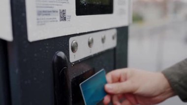 Yolcuların otobüs durağındaki şehir ulaşımı için bilet alırken görüntüsü kesilmiş. Erkek ellerine yakın çekim. Banka kartı ve bilet makinesiyle seyahat için ödeme yapıyorlar.