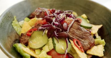 Etli salata, fasulye, vişneli domates, salatalık, kırmızı biber, kırmızı soğan, lahana salatası, beyaz arka planda dönen büyük tabakta nachos cipsi. Taco salatası. Kapat..