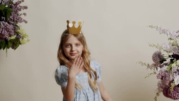 明るいブルーのドレスと金の王冠の7歳の少女は幸せで スタジオの白い背景に仮想キスを送ります カメラを見て優しく微笑んでいる美しい少女 — ストック動画