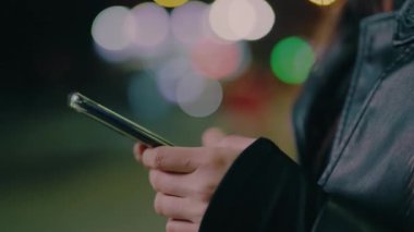 Genç bir kadın, gece geç saatlerde akıllı telefondan şehir sokağında duran bir mesaj atıyor. Şehirde dikilirken telefonu elinde tutan ve kullanan bir kadının fotoğrafı. Çevrimiçi iletişim.