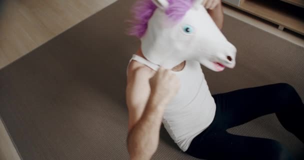 一个戴着独角兽面具的有趣男人在家里做运动来放松自己的肌肉 在家里的滑稽健身 健康与健康的概念 午餐休息时的背痛 — 图库视频影像