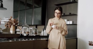 Genç ve güzel bir kadın evdeki modern mutfak odasında kahve ve çay içiyor. Sağlıklı sakin bir bayan minimalist yemek odasında dinleniyor. Evde tek başına stressiz hisset. Kadın evinde dinleniyor..