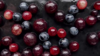 Siyah bir yüzeye yerleştirilmiş meyve, kızılcık ve yabanmersini. Mor ve mavi renkler mücevherlere benzeyen güzel bir desen oluşturuyor.