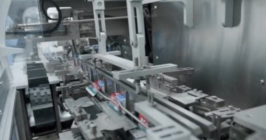 Bir makine, bir fabrika binasının içindeki taşıma bandındaki kutuların hareketini otomatikleştiriyor. Modern üretim teknolojisinin mühendislik harikasını gösteriyor.
