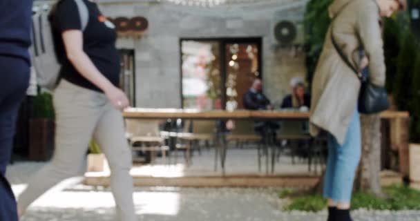 フラワーポットで飾られたアウトドアテーブル付きの賑やかなレストラン 歩行者が通り抜け 活気あふれる都市の雰囲気を捉えるパトロン — ストック動画