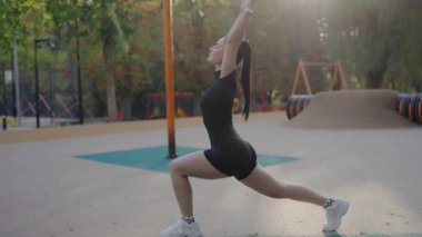 Spor giyim sektöründe odaklanmış genç bir kadın gün batımında huzurlu bir açık hava parkına atlıyor. Park 'ta Açık Hava Esneme Egzersizi Yapan Genç Kadın