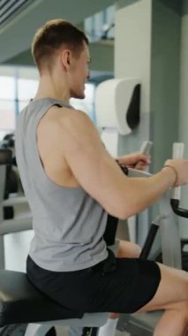 Genç Adam Modern Spor Salonunda Kas Yapmaya Odaklandı. Spor salonunda kürek çeken genç bir erkek sporcu, azim ve gücü gösteren fitness hedeflerine odaklanmış. Dikey video.