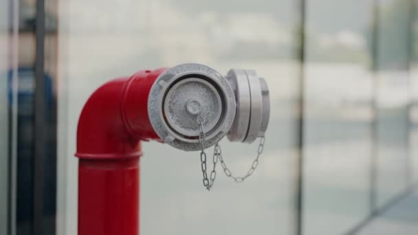 明るい都市背景に位置するダストキャップとセキュリティチェーンが装備されている赤い消火栓の詳細な画像 都市設定におけるダストキャップとチェーンの赤い消火栓のクローズアップ — ストック動画