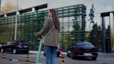 Genç bir bayan profesyonel, açık yeşil bir çanta taşıyan gösterişli bir şehir manzarasında güvenle ilerler. Modern Şehir Ortamı 'nda Şık Genç Kadın Yürüyüşü