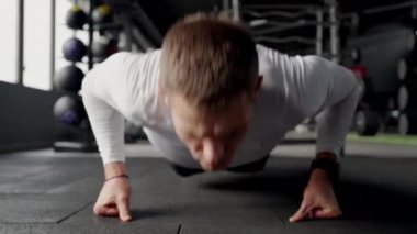 Atletizm kıyafetleri içinde odaklanmış beyaz bir erkek iyi donanımlı bir spor salonunda şınav çeker, gücünü ve bağlılığını gösterir. Modern Spor Salonunda Şınav çeken Odaklanmış Genç Adam