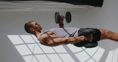 23 yaşındaki atletik bir adam bir stüdyoda yoğun bir fiziksel antrenman yapıyor. Egzersiz yaparak gücünü ve dayanıklılığını gösteriyor. Dikey video. Genç Atletik Adam Güç Alıştırmaları Yapıyor.