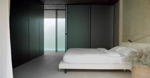 一间宽敞而简约的卧室 有一张白色床上用品的大床 从地板到天花板的黑暗储物柜和巨大的玻璃窗 这个房间把雅致的现代设计与舒适结合起来 — 图库视频影像
