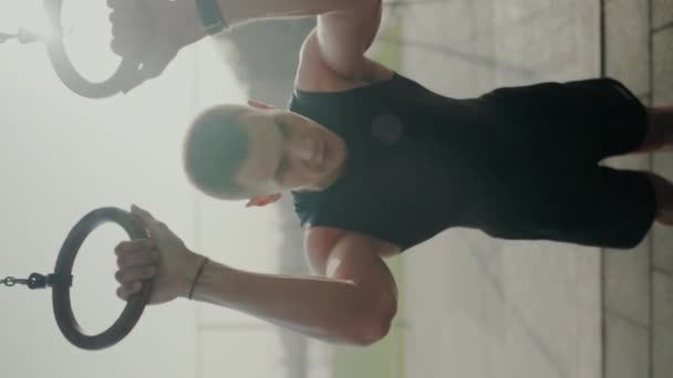以年轻男性运动员为重点 在健身房使用体操圈 在柔和灯光下展示力量和注意力集中 年轻男子运动员在健身房进行体操环运动 垂直录像 — 图库视频影像
