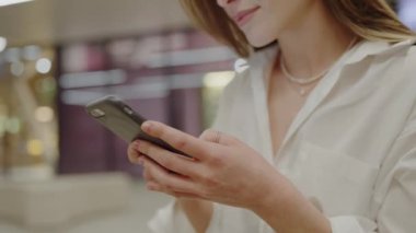 Parlak bir alışveriş merkezinde akıllı telefonunu kullanan hoş bir gülümsemesi olan çekici genç bir kadın. Alışveriş merkezinde akıllı telefonuyla mesajlaşan genç bir kadın.