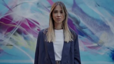 Kendine güvenen, şık bir spor ceket giyen genç profesyonel bir kadın, şehir ortamında canlı bir grafiti duvarına karşı poz veriyor. Şehirdeki Profesyonel Kadın Pozisyonu Renkli