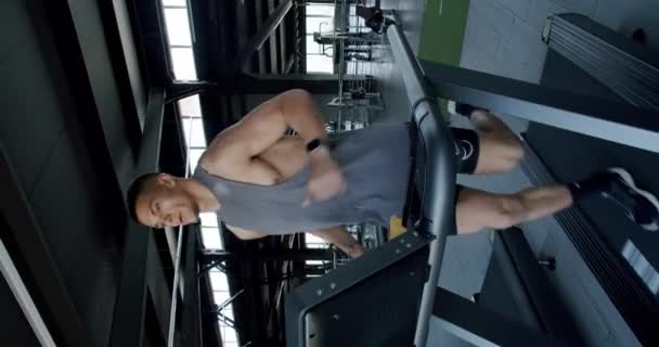 モダンジムのトレッドミルで意図的に走る若い筋肉男 筋肉のビルドを持つ若い男性は 彼のトレーニングの強度に焦点を当て ハイテクジムでトレッドミルを実行します バーティカルビデオ ストック動画