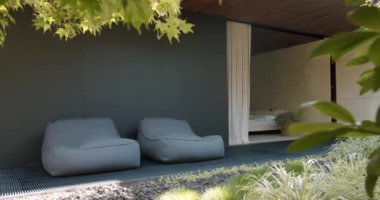 Zarif modern ev dış görünüşü. Gölgeli bir verandanın altında iki şık puf minder bulunan dinlendirici bir salon. Sıcak ve huzurlu bir yer huzurlu öğleden sonraları için mükemmel. Modern Açık Hava Salonu Alanı