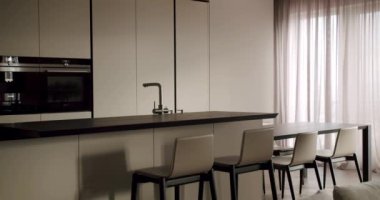 Pürüzsüz ve şık bir minimalist mutfak, entegre cihazlar ve uzun bir masa ve şık sandalyeler içeren bir yemek alanı, hepsi de yumuşak nötr tonlarda. Modern Minimalist Mutfak ve Yemek Alanı