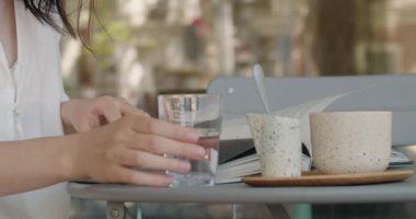 Kapalı bir kafede dergi okurken elinde bir bardak su tutan genç bir kadının el resmi. Ayrıca kahve fincanı ve çay tabağı da var..