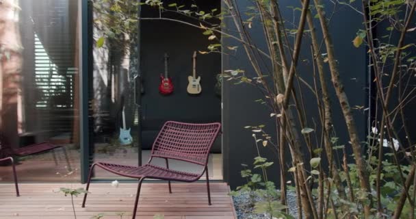 一种舒适时髦的户外庭院 其特点是在黑暗的墙上挂着一张织成的红色椅子 木制甲板和吉他手 四周环绕着绿色的植物 雅致的座位 别致的户外耐心 — 图库视频影像