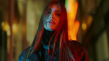 Işıkların arkasında kameraya poz veren güzel bir kadın. Gece lambalarının arka planına karşı genç bir kadın. Şehir, gece, ışık, dışarıda, akşam, yaşam tarzı, ayakta.