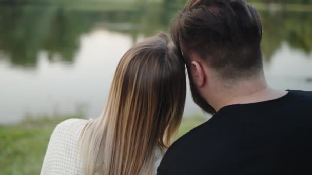 落ち着いた湖で一緒に座っているロマンチックなカップルのバックビューは 愛と仲間の感覚を反映して 平和的な夕日を鑑賞します サンセット湖でセレンモーメントを楽しむカップル ロイヤリティフリーのストック動画