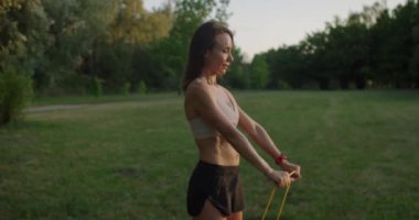 Sportif kadın dışarıda antrenman yapıyor ve elinde direniş bandıyla antrenman yapıyor. Atletik kadın sabah güneş doğarken dışarıda egzersiz yapıyor. Spor kıyafetli bir kadın direniş bandı egzersizleri yapıyor..