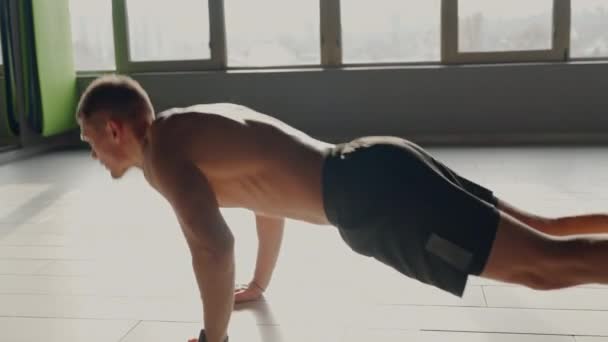 一个强壮的运动健将在阳光下沐浴的健身房地板上做俯卧撑 图像显示了力量 耐力和锻炼的焦点 日光浴体操中心男子运动员推杆专项表演 — 图库视频影像