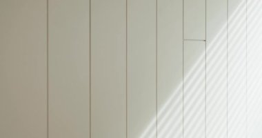 Yumuşak ışıklandırmanın altındaki beyaz tahta panellerin yakın plan çekimi çizgilerle kesişen gölgeler minimalist bir estetik oluşturuyor. Işık ve Gölgeler Oynayan Minimalist Beyaz Duvar Panelleri