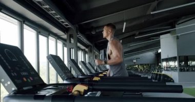 Modern Spor Salonu 'nda Koşu bandına odaklanmış genç adam. Çağdaş bir spor salonunda koşu bandında koşan genç bir sporcu azim ve zindelik gösteriyor..