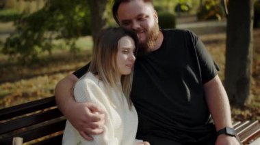 Genç bir çiftin sonbahar yapraklarıyla çevrili bir bankta otururken hassas bir anı paylaştığı yürek ısıtan bir sahne. Sonbaharda Park Benç 'ine Kucaklayan Genç Çift