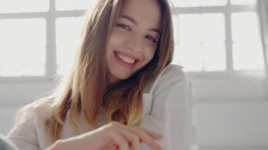 Neşeli genç bir kadının portresi. Işıl ışıl gülümseyen, kapalı alanda güneşli bir günün tadını çıkaran. Onun ifadesi mutluluk ve pozitiflik taşır. Doğal Işıkta Parlak Gülümseyen Mutlu Genç Kadın