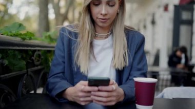 Bir iş kadını kafeterya masasında kahve fincanı görünür bir şekilde otururken akıllı telefonunu kullanır. Modern bağlantılara ve devam eden işlere odaklan. İş kadını Kafe 'de Kahveyle Açık Mesaj Yazıyor 