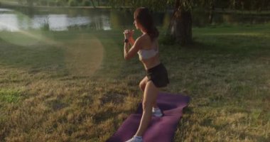 Tek başına spor kadın eğitimi. Çekici, zayıf vücutlu, sportif bir kadın. Sağlıklı bir yaşam tarzı ve parkta eğitimi var. Kadın yan hamleler yapıyor, dışarıda egzersiz yapıyor. Atletik sarışın kasları eğitir.