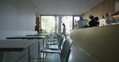 Modern bir kahve dükkanının içinde müşterilerin olduğu bir manzara, modern mobilyalar ve sıcak, davetkar bir atmosfer. Temiz çizgiler ve doğal ışık minimalist tasarımı tamamlar.