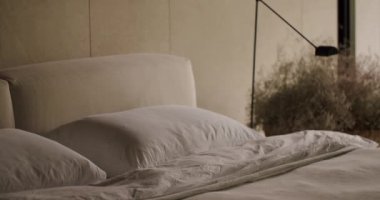 Lüks bir yatakta yumuşak yastıklar ve ev dekorasyonu için mükemmel modern bir lamba bulunan sakin bir yatak odası. Yumuşak Yastıklar ve Modern Lambalarla Zarif Yatak Odası İçi