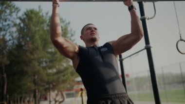 Odaklanmış genç bir adam, doğal bir ortamda zindelik, kararlılık ve güç göstererek barfiks egzersizi yapar. Genç adam güneşli bir günde dışarıda antrenman yapıyor, Kararlılık ve Güç