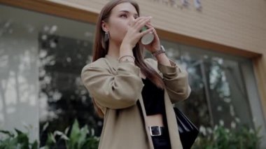 Şık bir genç kadın, şehir bahçesinde kahve içmekten hoşlanır. Şık kıyafeti ve odaklanmış ifadesi modern hayat ve zarafeti çağrıştırır..