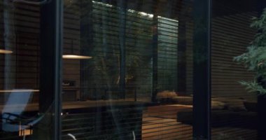 Gece şık evlerin oturma odasına huzurlu bir manzara, sıcak, parıldayan bir lamba ve büyük cam pencerelerin arkasında rahat mobilyalar. Parlak Mimari ve Ilık Işıklandırma